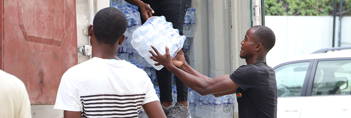 Two people move a case of water out of a truck.